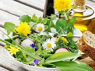 Ein Salat mit frischen Kräutern neben einer Flasche Olivenöl.