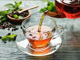 Eine Glastasse, die mit Tee aus einer Glaskanne gefüllt wird.