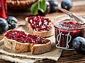 Marmeladenbrote und ein Glas Marmelade liegen neben ein paar Beeren auf einem Tisch.