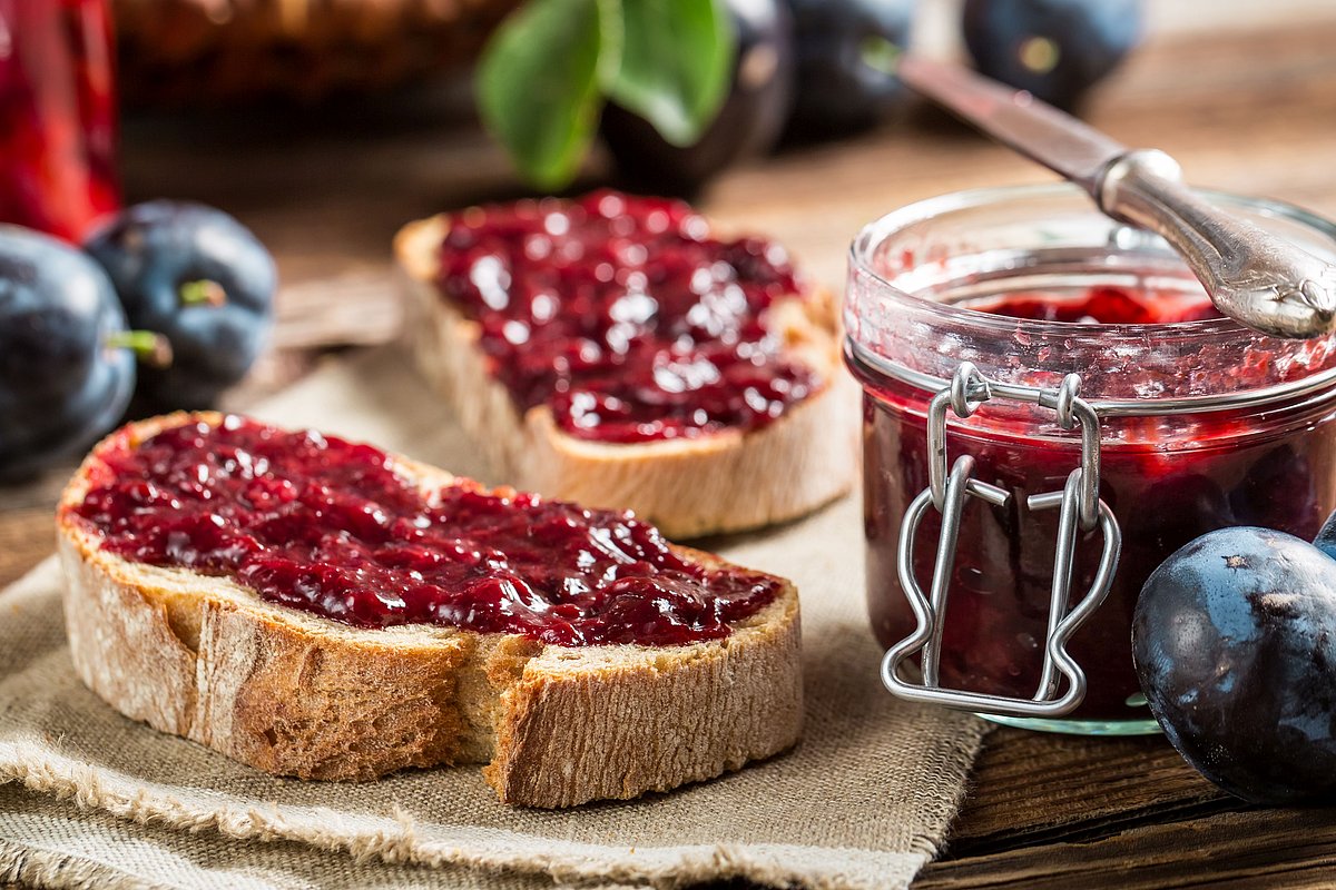 Marmeladenbrote und ein Glas Marmelade liegen neben ein paar Beeren auf einem Tisch.