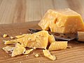 Ein Stück Hartkäse liegt auf einem Holzbrett neben einem Käsemesser.