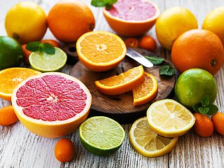 Verschiedene Zitrusfrüchte liegen zum Teil aufgeschnitten auf einem Holzbrett.