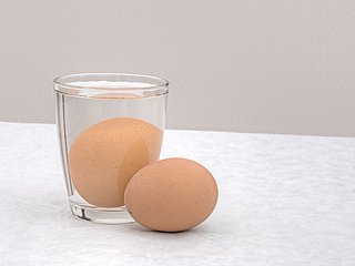 Ein braunes Ei in einem Glas, ein weiteres liegt daneben.