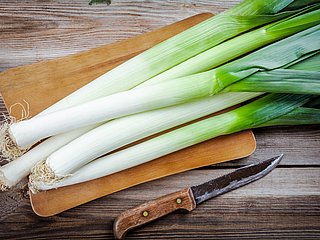 Mehrere Lauchstangen liegen auf einem Holzbrett. Daneben liegt ein Messer.