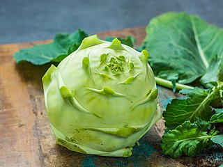 Ein Kohlrabi liegt neben Kohlrabiblättern auf einem Holzbrett.