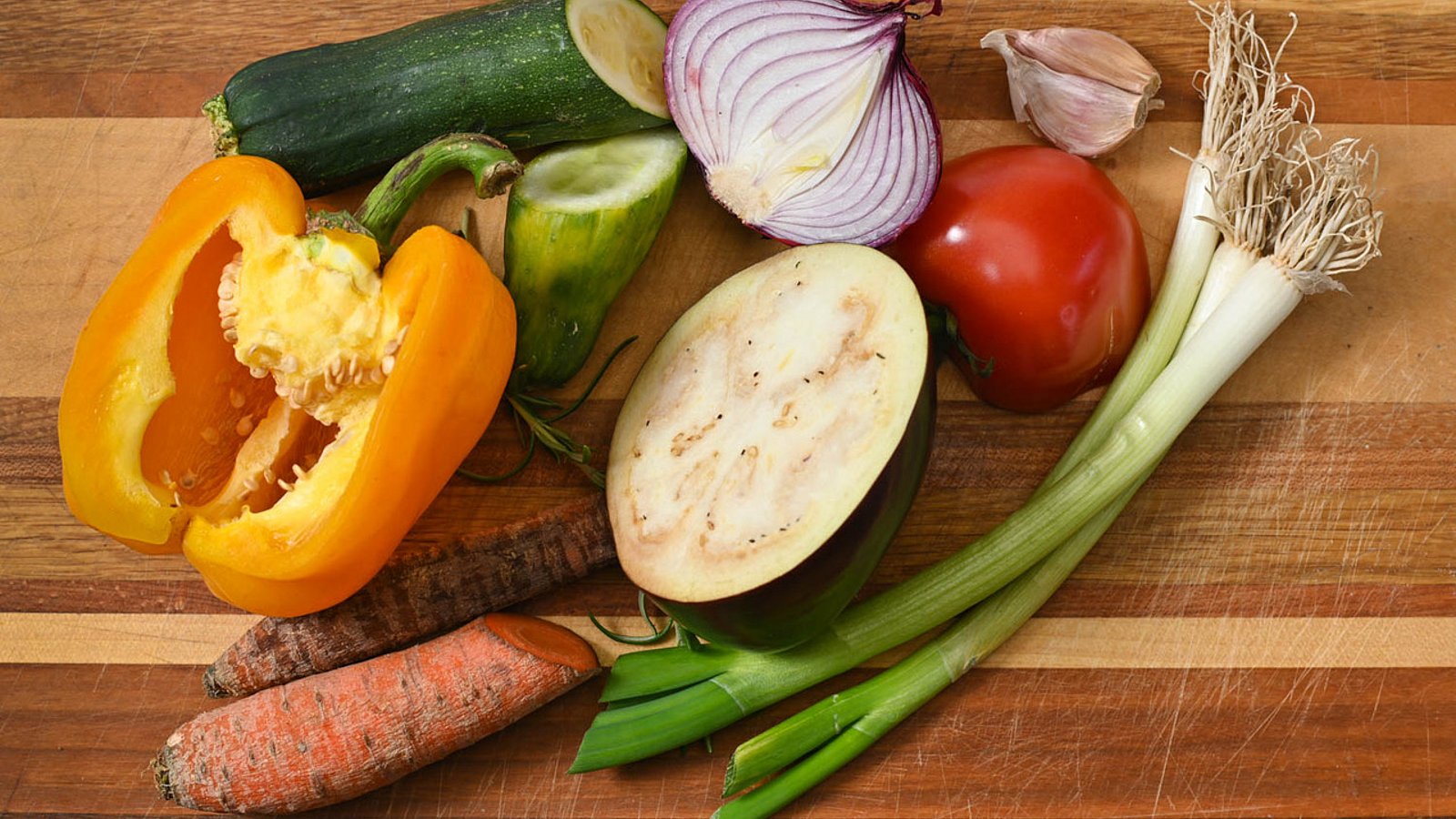 Paprika. Möhre, Lauchzwiebeln und weiteres Gemüse auf Holztischplatte, teilweise aufgeschnitten