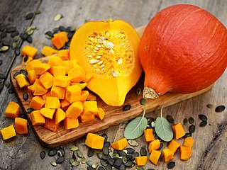 Ein ganzer und ein aufgeschnittener Kürbis auf einem Holzbrett.