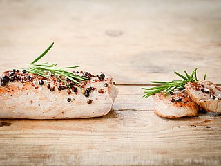 Mehrere Stücke gebratenes Schweinefleisch liegen garniert mit Gewürzen auf einem Holzbrett.