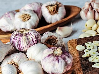 Mehrere Zehen Knoblauch liegen neben aufgeschnittenem Knoblauch.