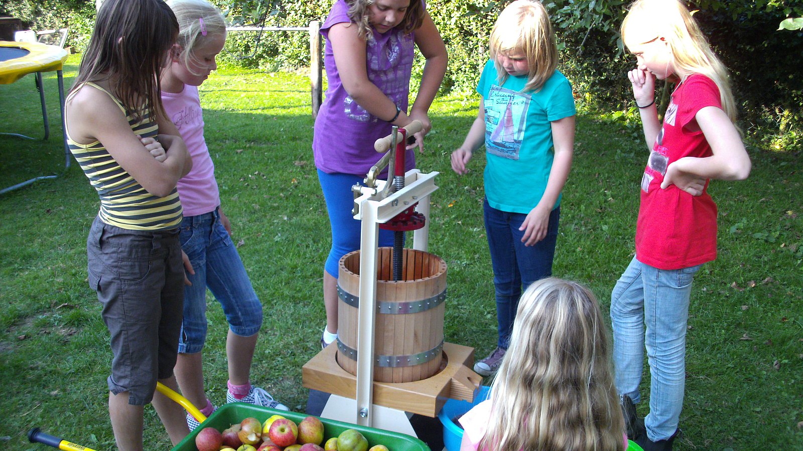 Mehrere Kinder stehen an und rund um eine Manuelle Apfelsaftpresse