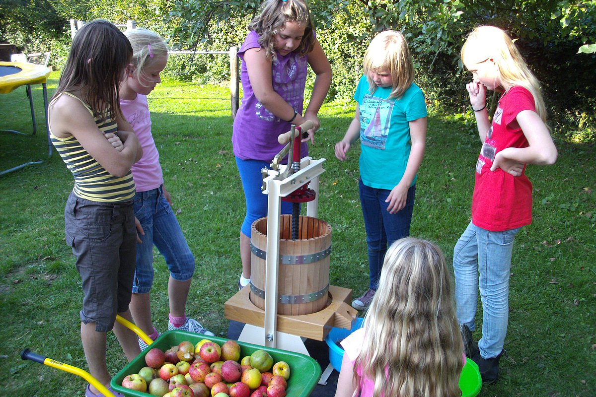 Mehrere Kinder stehen an und rund um eine Manuelle Apfelsaftpresse