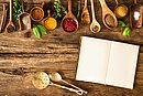 Auf einer Arbeitsplatte liegen verschiedene Gewürze und ein leeres Notizbuch.