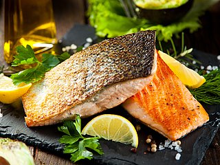 Zwei gebratene Fischfilets liegen auf einer Schieferplatte garniert mit Kräutern und Zitronen.