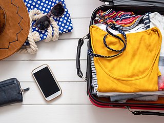 Ein offener, gepackter Koffer mit Kleidung und Accessoires.