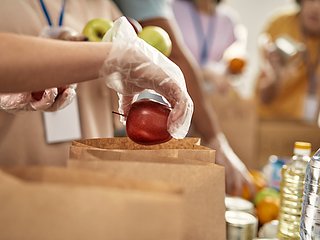 Eine Hand mit Plastikhandschuh, die einen Apfel hält.