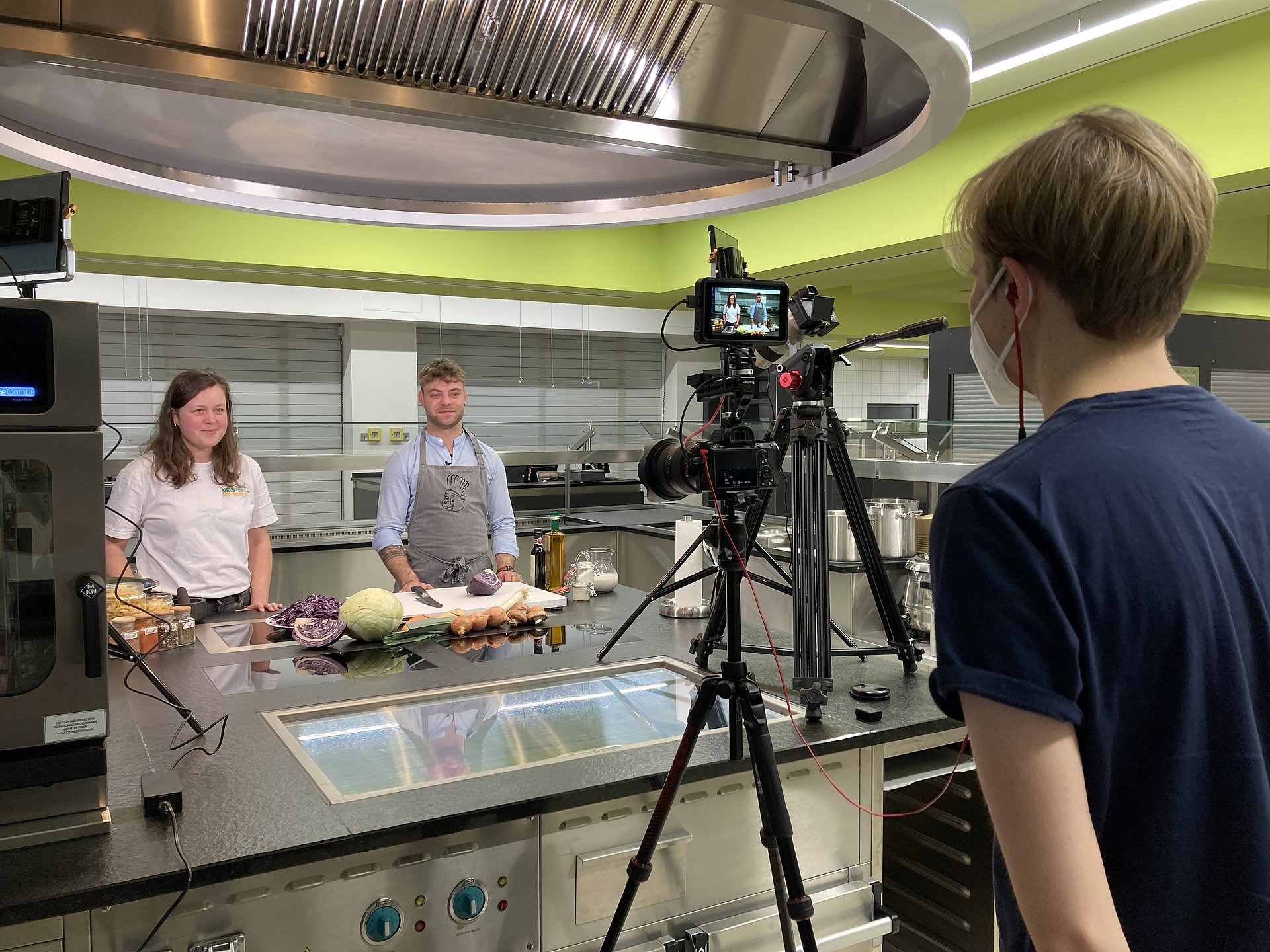 Zwei Personen stehen in der Mensa für ein Videodreh zu einem Kochkurs vor der Kamera.