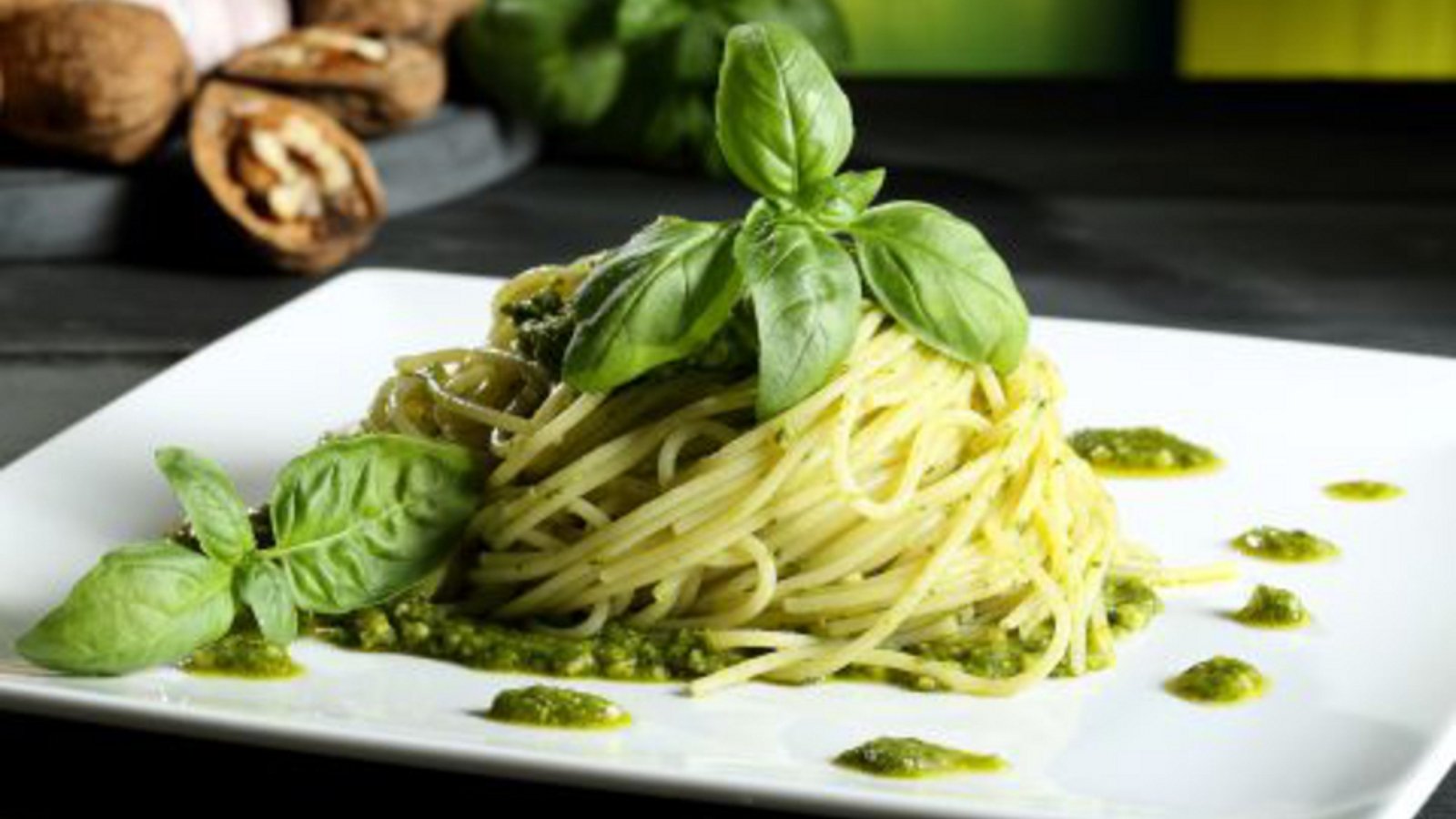 Schön angerichtete Spagetthi mit grünem Pesto, dekoriert mit Basilikumblättern 