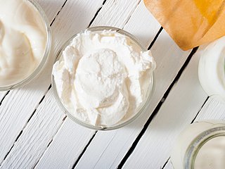 Eine Schüssel Quark und eine Schüssel Joghurt stehen neben einem Glas Sahne. 