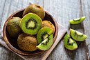 Einige Kiwis liegen, teilweise geschnitten, teilweise im Ganzen, in einer Holzschale.