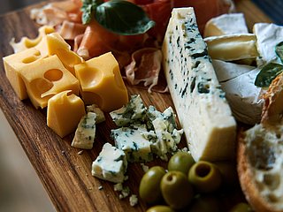 Verschiedene Käsesorten und Beilagen auf einem Holzbrett.