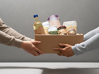 Eine box mit Lebensmitteln wird von einer Person an eine andere gegeben.