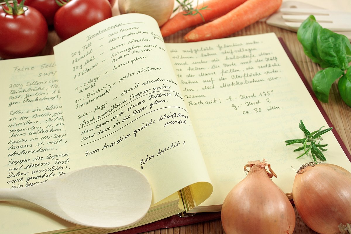Handgeschriebenes Kochbuch liegt aufgeschlagen da, rundherum Gemüse und Kochutensilien