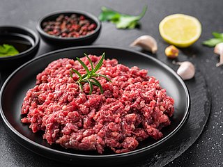 Rohes Hackfleisch liegt auf einem Teller. Daneben stehen kleine Schüsseln mit Gewürzen.