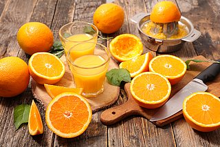 Aufgeschnittene Orangen und frisch gepresster Orangensaft in Gläsern auf einem Holztisch.