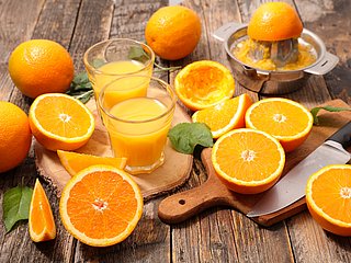 Aufgeschnittene Orangen und frisch gepresster Orangensaft in Gläsern auf einem Holztisch.