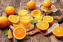 Aufgeschnittene Orangen und frisch gepresster Orangensaft in Gläsern auf einem Holztisch.