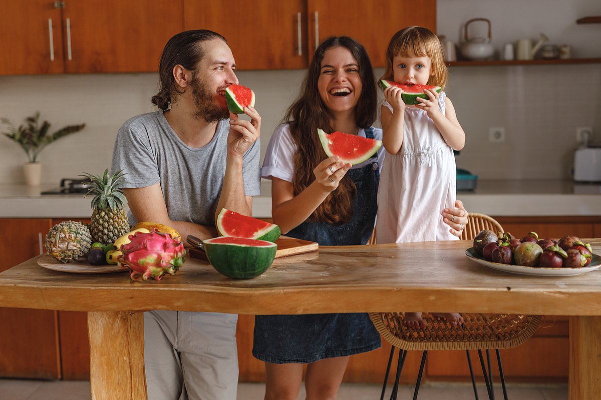 Ein kleines Kind isst mit seiner Mutter und seinem Vater Wassermelone in der Küche.