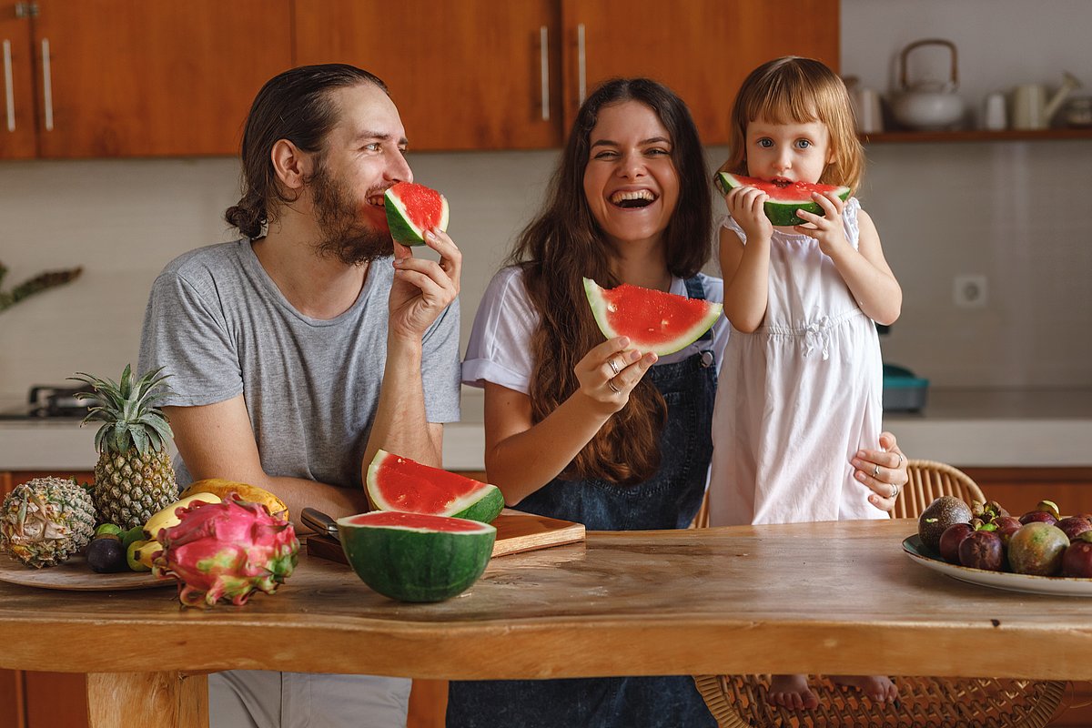 Ein kleines Kind isst mit seiner Mutter und seinem Vater Wassermelone in der Küche.