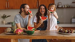 Ein kleines Kind isst mit seiner Mutter und seinem Vater Wassermelone in der Küche.