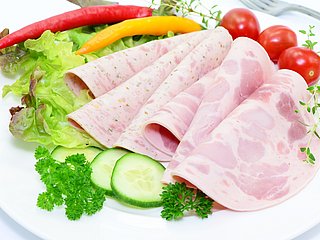 Wurstaufschnitt ist auf einem Teller drapiert und garniert von Gemüse. 