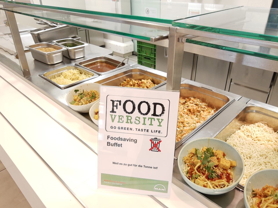 Ein Schild mit der Aufschrift "Foodversity Go Green. Taste Life" vor einem Buffet