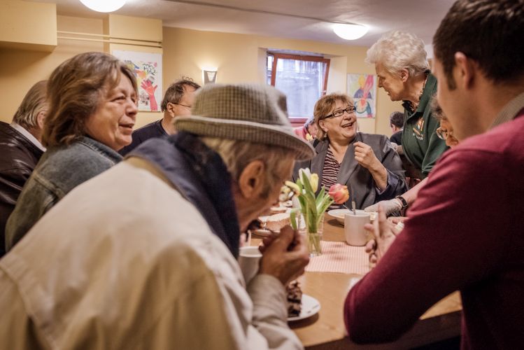 Mehrere Menschen sitzen zusammen an einem Tisch. Sie haben Tassen und Teller mit Kuchen vor sich.