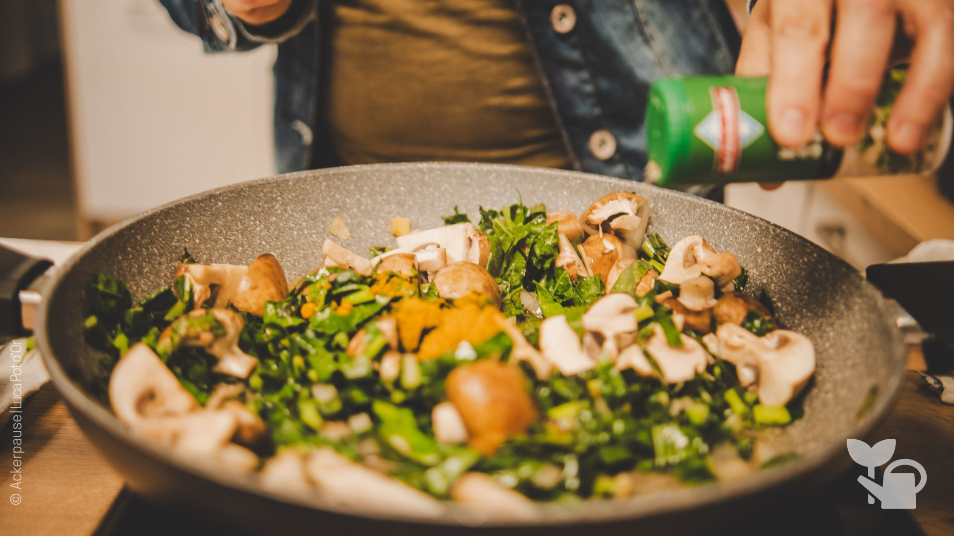 Eine Person würzt eine Pfanne mit einem Gericht aus verschiedenem Gemüse. 
