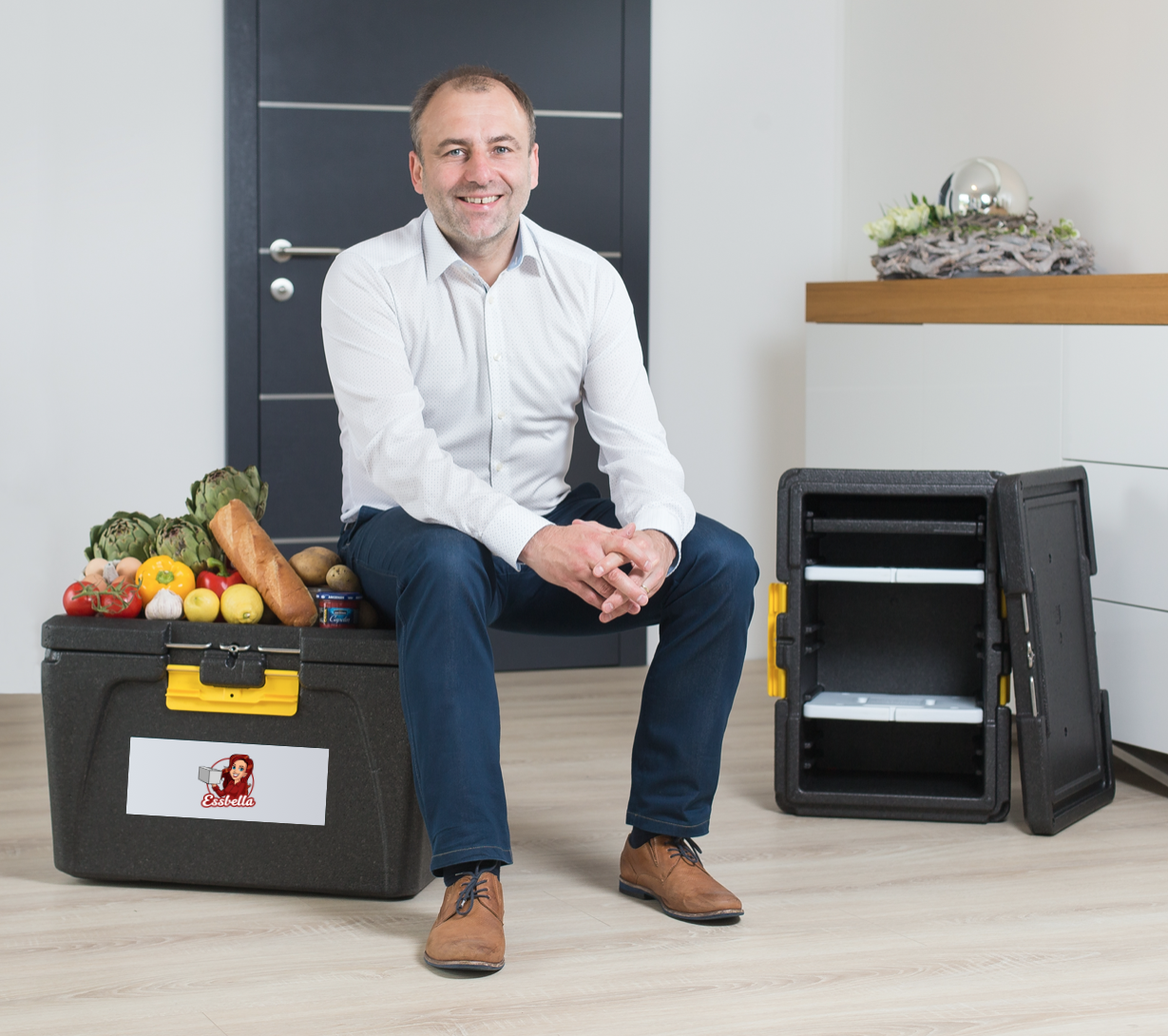 Das Bild zeigt Estella Gründer und Geschäftsführer Adrian Lissy (ca.50 Jahre alt), der in einem Büro auf einer Gemüsekiste sitzt und nett in die Kamera lächelt.