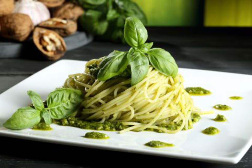 Schön angerichtete Spagetthi mit grünem Pesto, dekoriert mit Basilikumblättern 